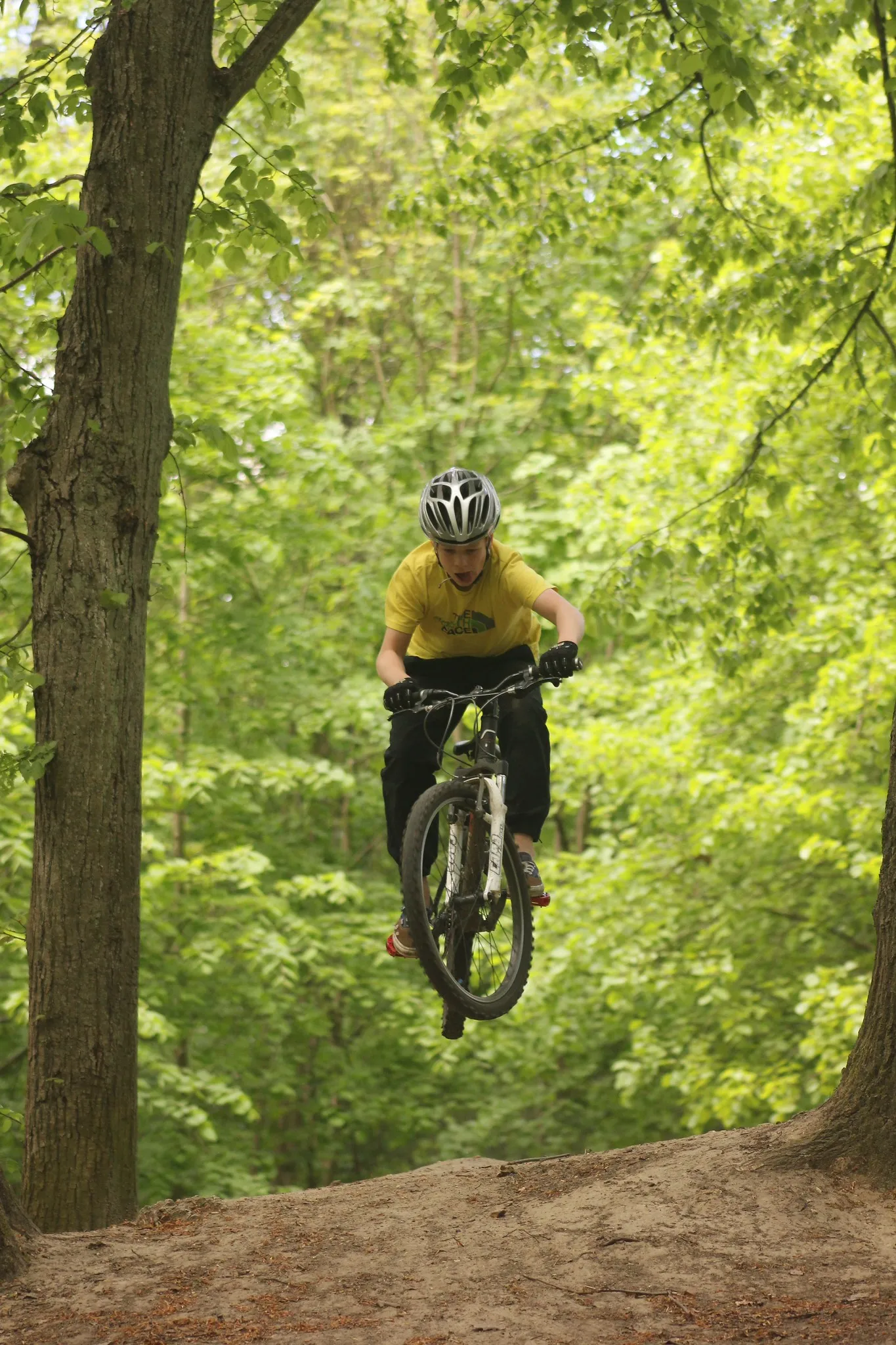 A mountain biker in a yellow top in the air above a dirt jump