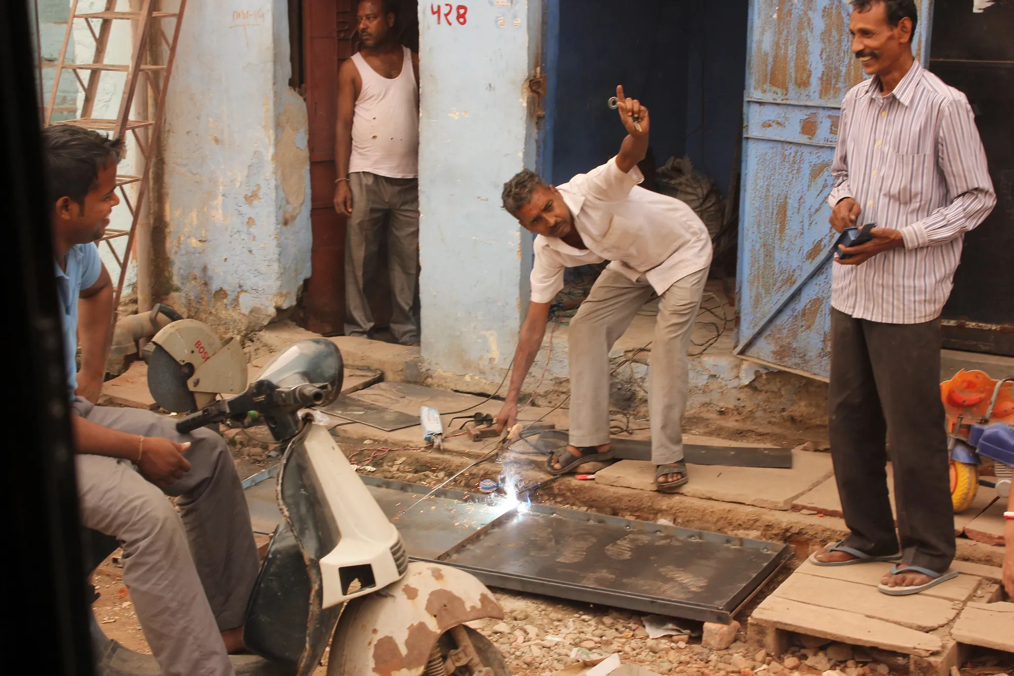 A man welding a metal sheet on a street while others watch