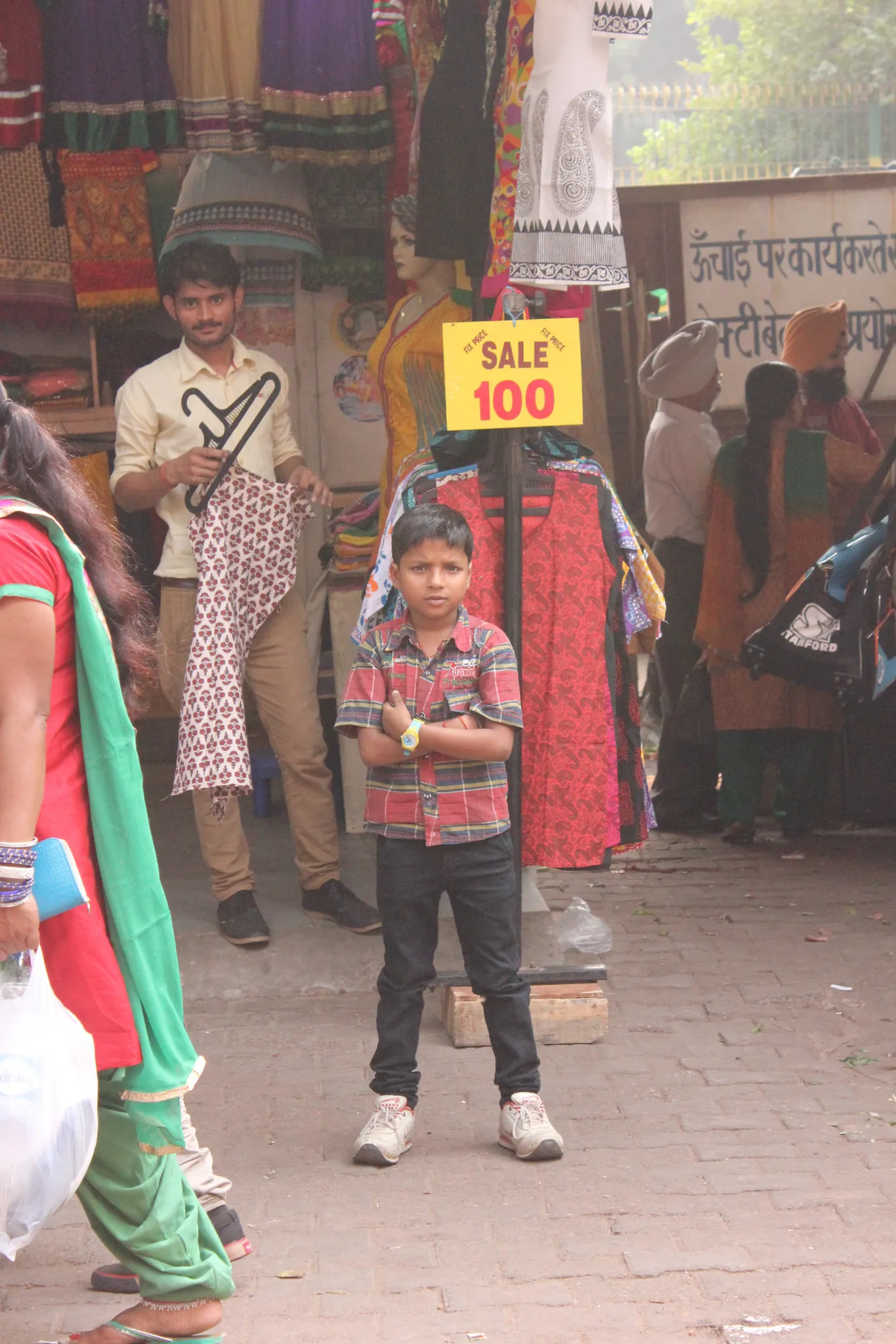 A boy standing outside a clothes stall with a sale sign