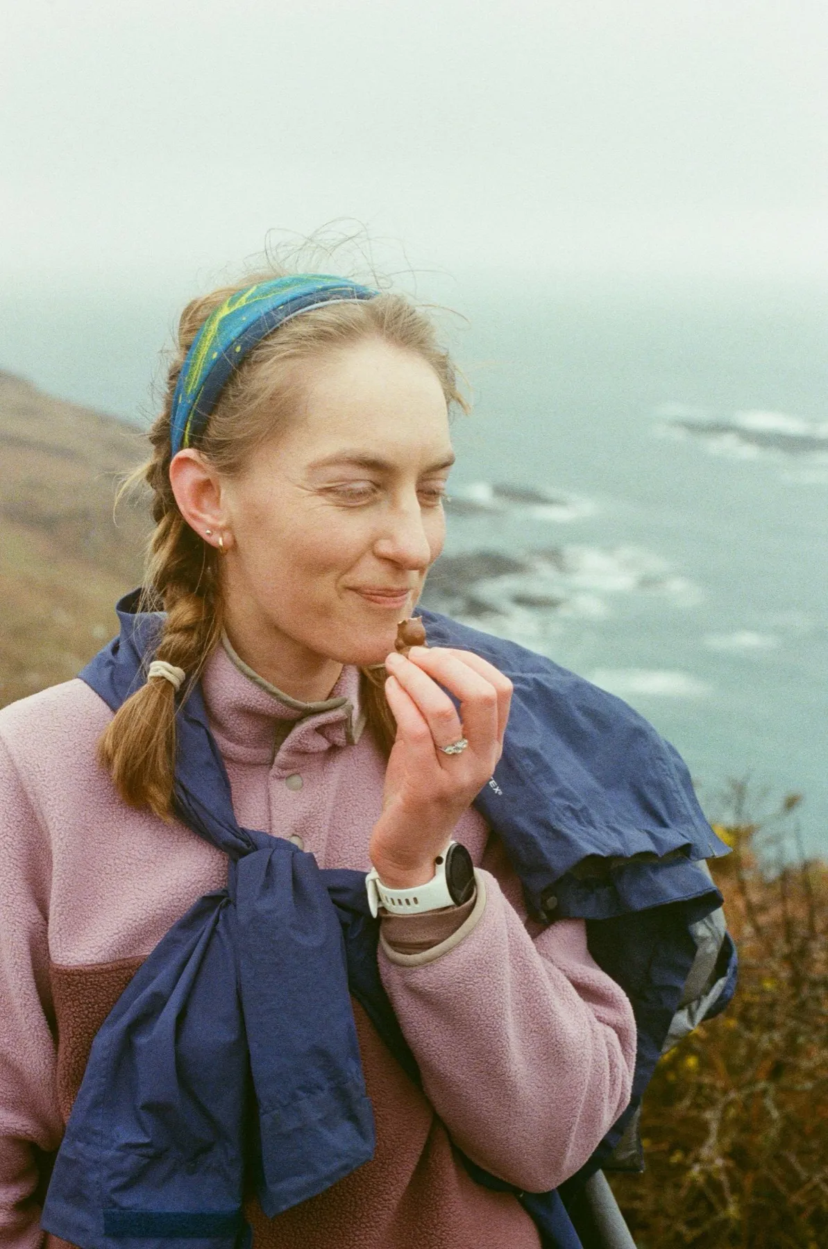 Film photograph: a woman eating chocolate on a clifftop above the sea in Cornwall