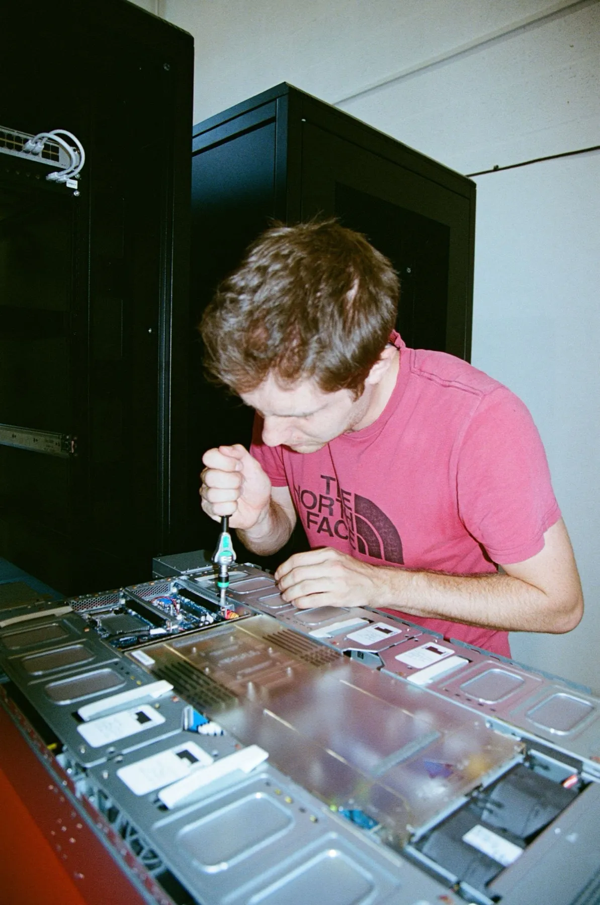 Film photograph: Sam, in a pink T-shirt, working inside a server with a Wera screwdriver